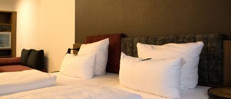 Habitación de hotel con dos camas, ropa de cama blanca, cabecera marrón y una mesita de noche de madera.