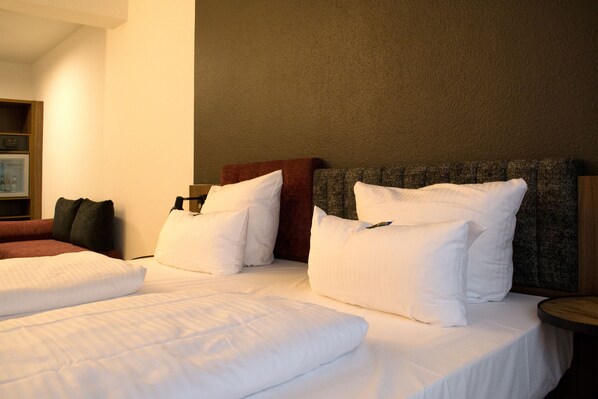 Habitación de hotel con dos camas, ropa de cama blanca, cabecera marrón y una mesita de noche de madera.