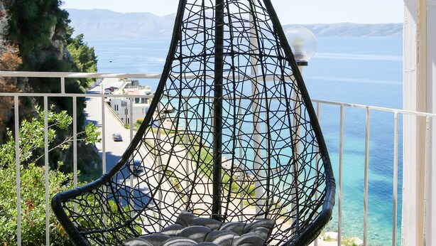 Una silla colgante en un balcón con vista al mar y edificios.