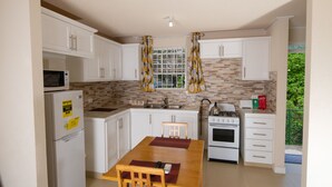 A compact kitchen with white cabinets, a microwave, a stove, and a sink. - THE Cottage, Saint Davids, Christ Church, Barbados (Oistins)