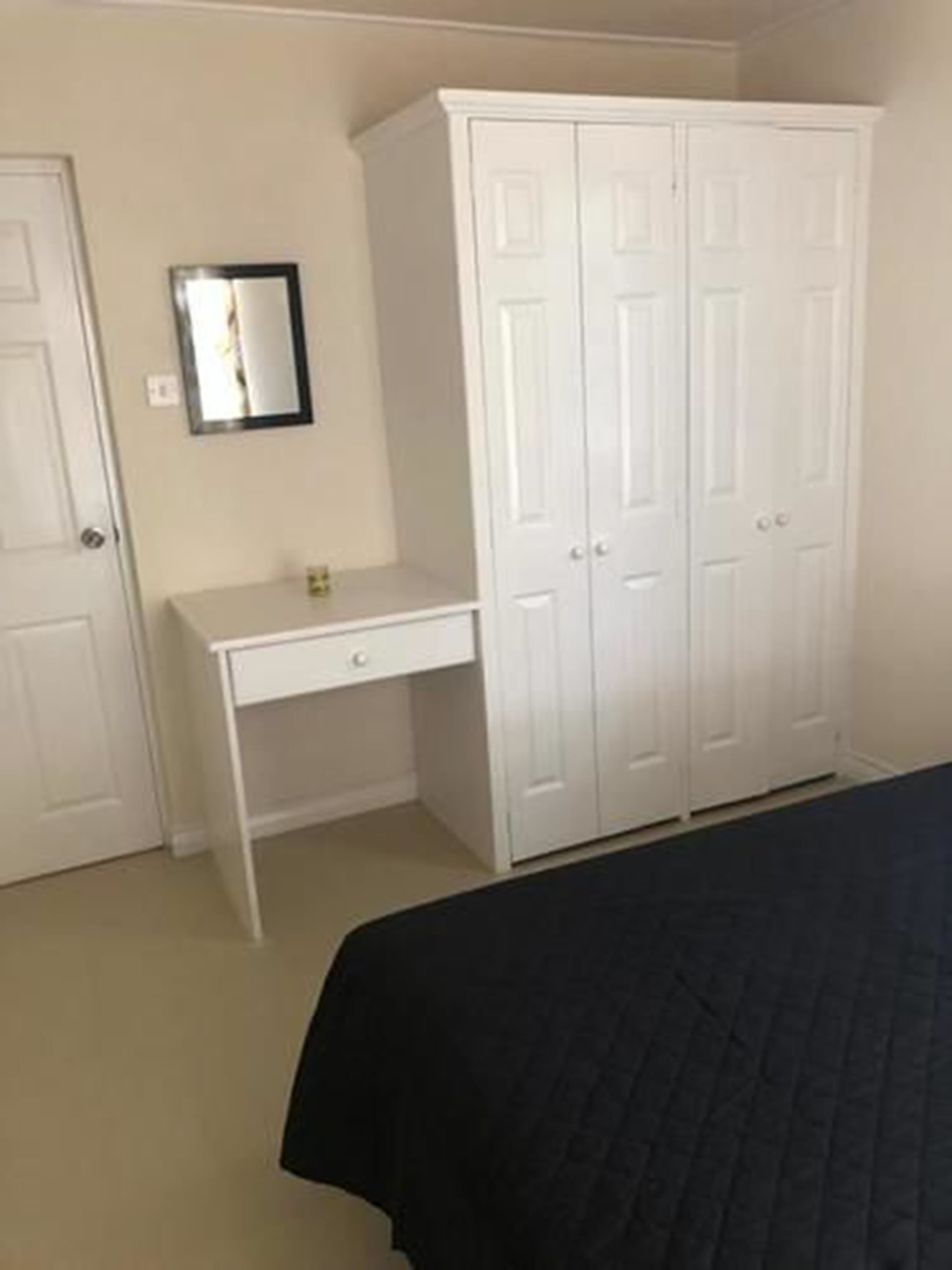 A bedroom with a bed, a white desk, and a wardrobe.