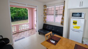 A compact kitchen with a dining area, a black leather sofa, and a small table with a remote control. - THE Cottage, Saint Davids, Christ Church, Barbados (Oistins)