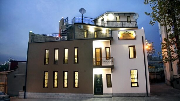 Un bâtiment à deux étages doté d’un balcon à l’étage supérieur, d’une antenne parabolique sur le toit et d’une entrée éclairée.