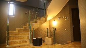 Un escalier avec une rampe en verre, un petit pouf et un luminaire fixé au mur.