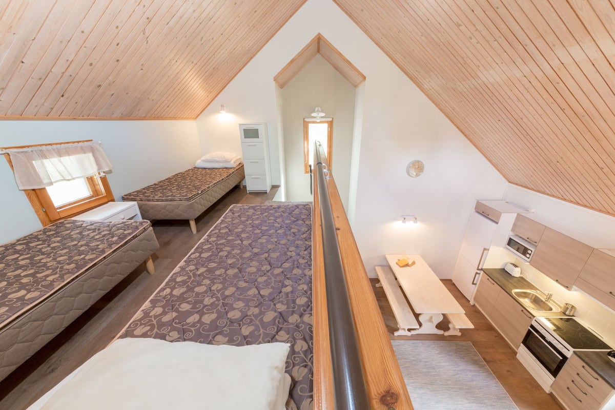A compact, well-lit attic bedroom with two beds, a kitchenette, and a small bathroom.