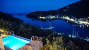 A waterfront property with a swimming pool, boats docked at the marina, and a view of the surrounding hills. - Ktima Aniforeli Luxury Villas (Lefkada)