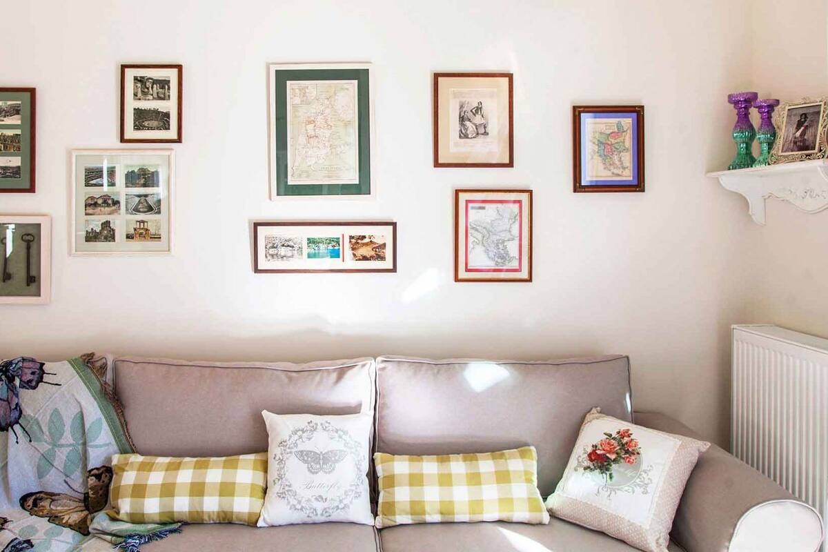 A living room with a beige sofa, a patterned throw, and various framed pictures on the wall.