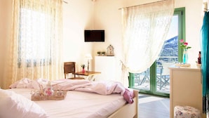 A bedroom with a bed, a desk, a chair, a TV, and a view of the outdoors. - Ktima Aniforeli Luxury Villas (Lefkada)
