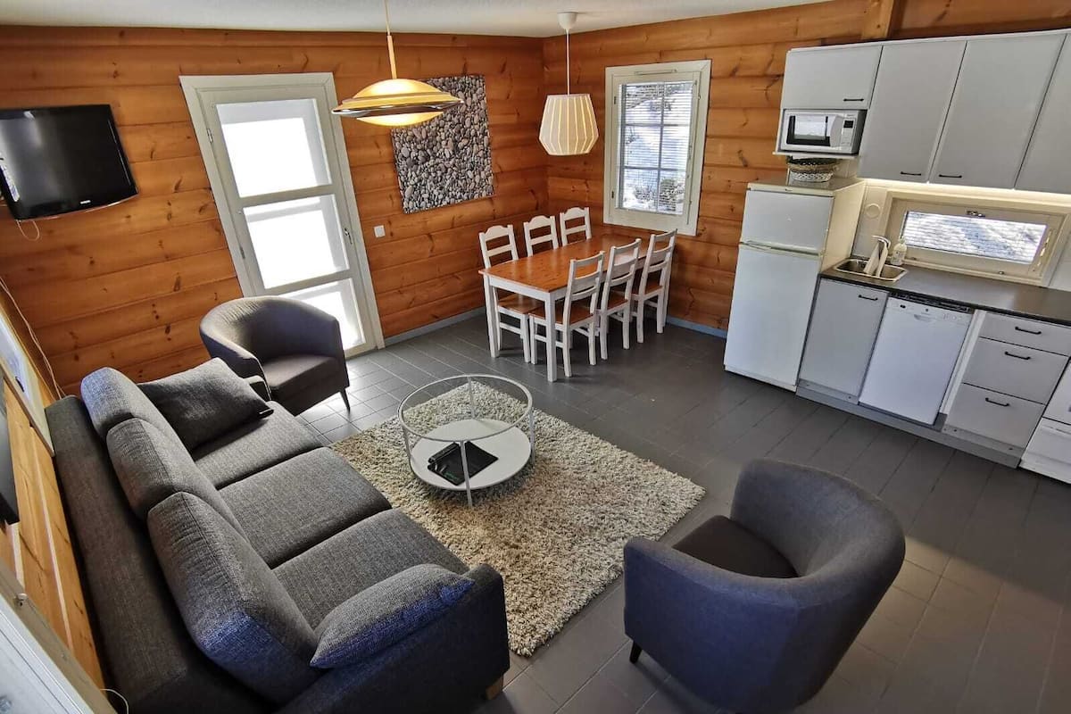 A compact living space with a sofa, armchair, dining table, and kitchen area.