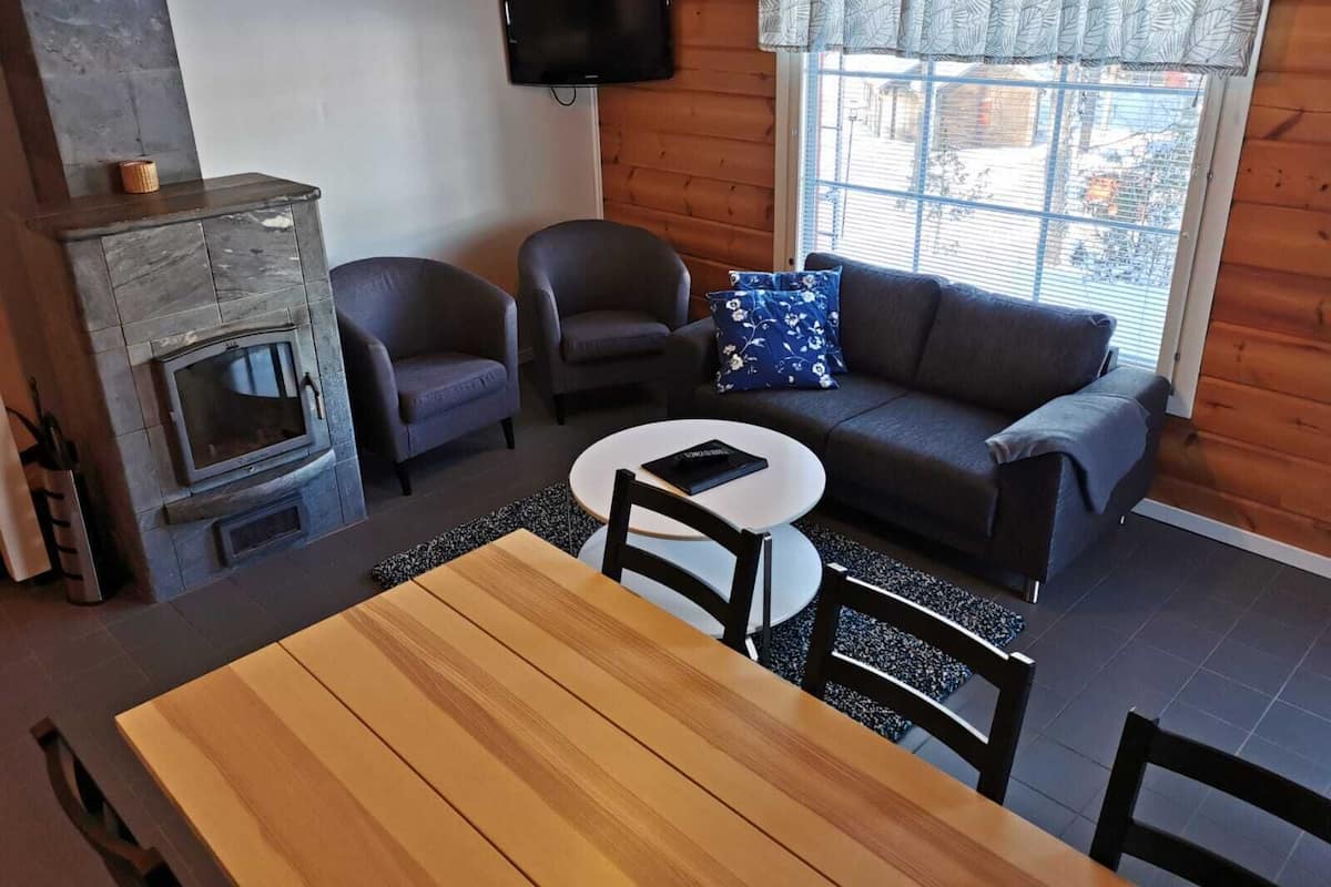 A cozy living room with a fireplace, a sofa, two armchairs, a TV, and a dining table.