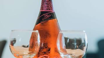 Una botella de vino espumoso Boheme, una rosa y dos copas sobre una mesa con un cartel de Rhodesfentai.gr.