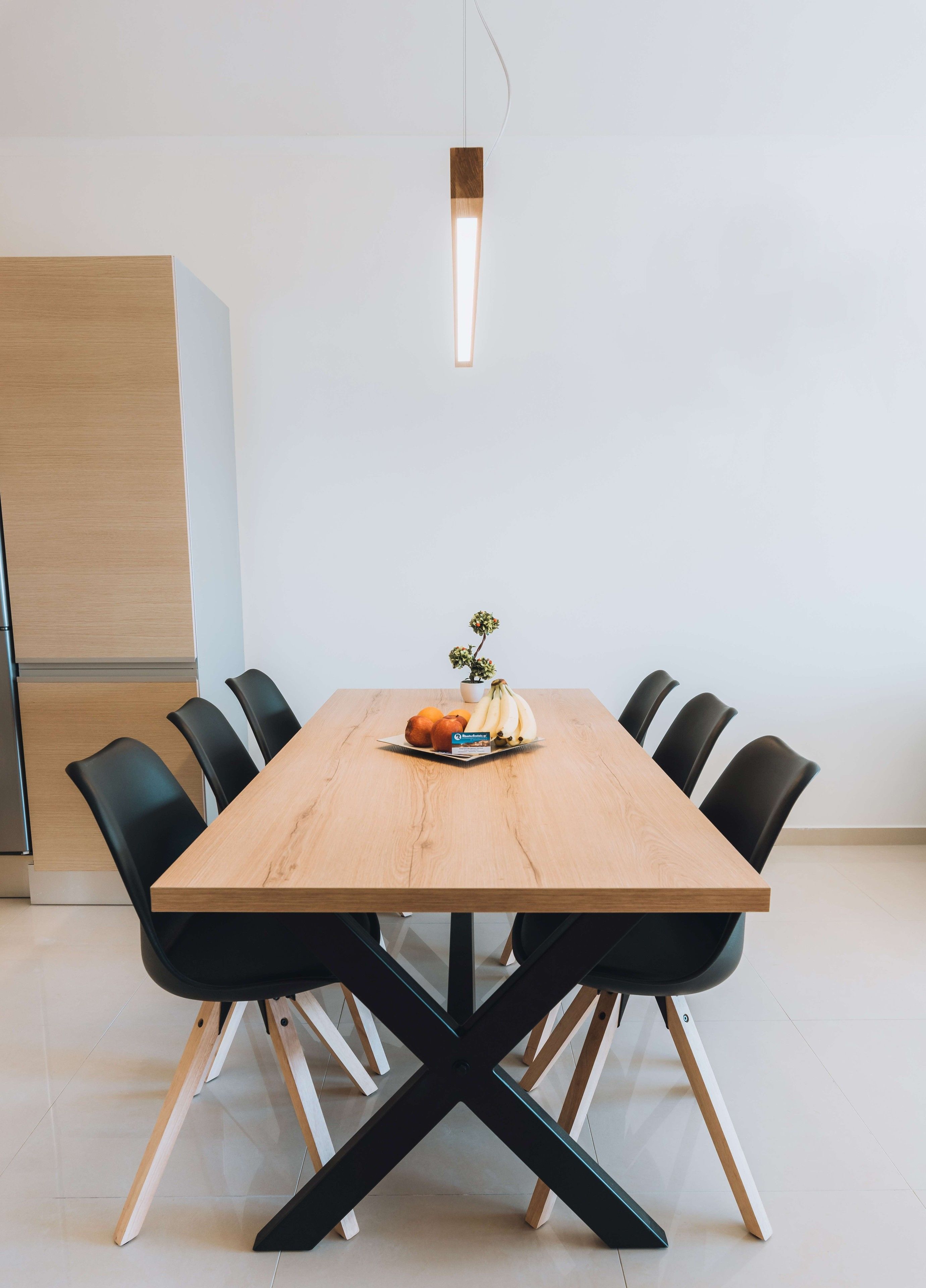 Uma mesa de jantar moderna com cadeiras pretas, chão de madeira e uma pequena planta em vaso sobre a mesa.