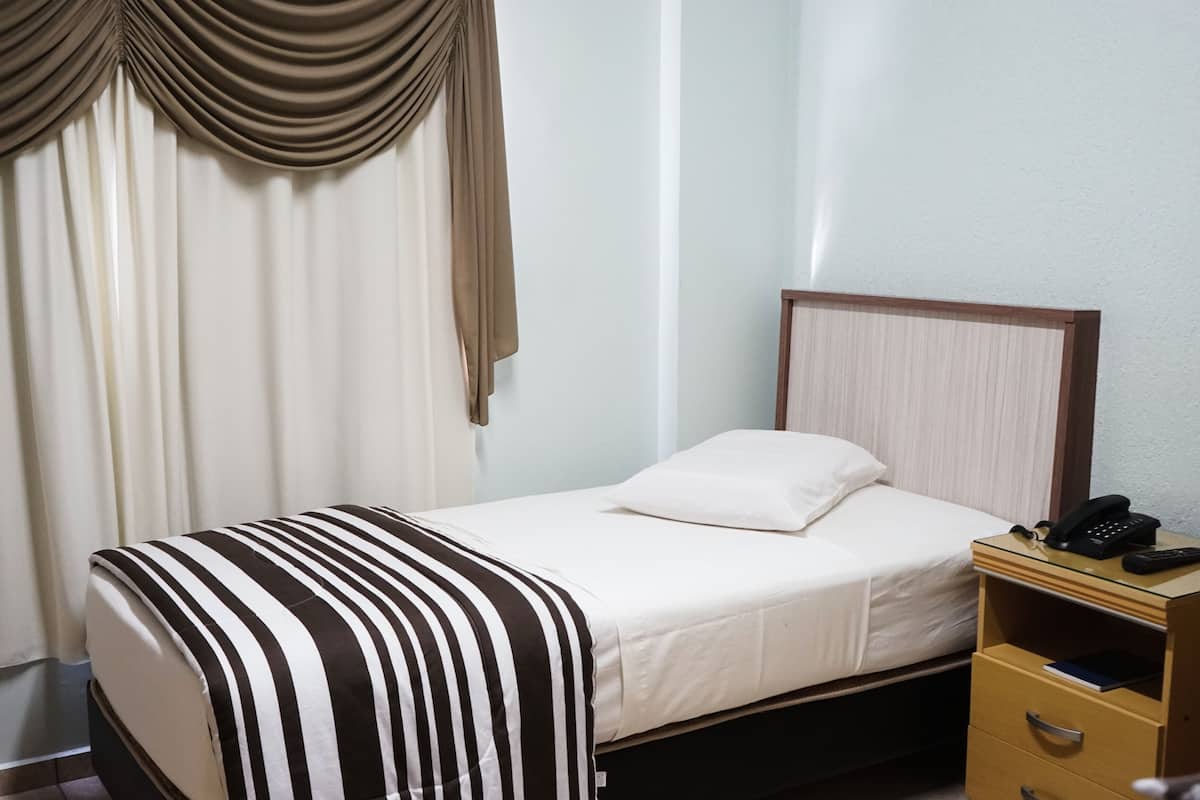 A hotel room with a bed, a bedside table with a phone, and a window with curtains.