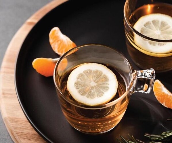 Two clear glasses of amber liquid with a slice of lemon, placed on a black tray with a wooden edge.