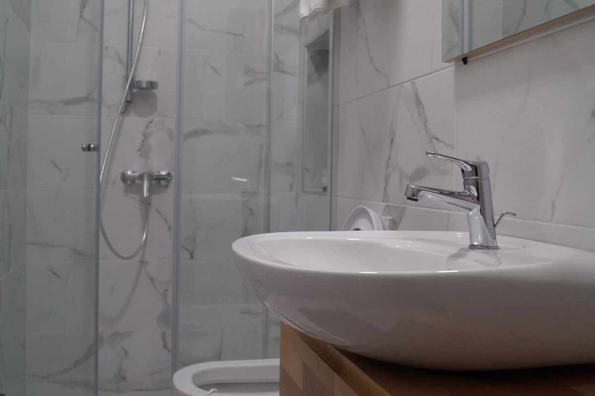 A bathroom with a glass shower enclosure, a toilet, a sink with a wooden vanity, and a towel rack with folded towels.
