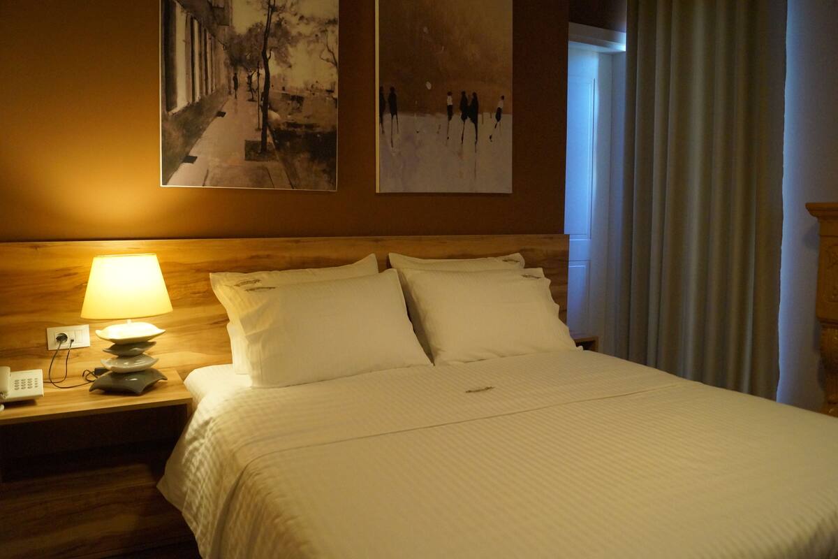 A hotel room with a large bed, a bedside lamp, a nightstand with a phone, and artwork on the wall.