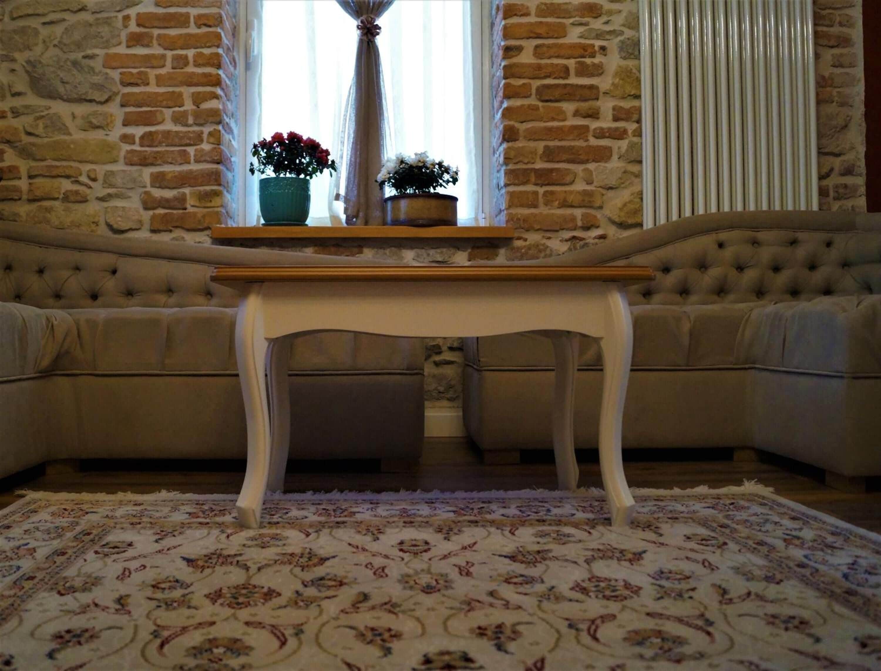 Una habitación con pared de ladrillo, sofá color beige, mesa blanca y alfombra estampada.