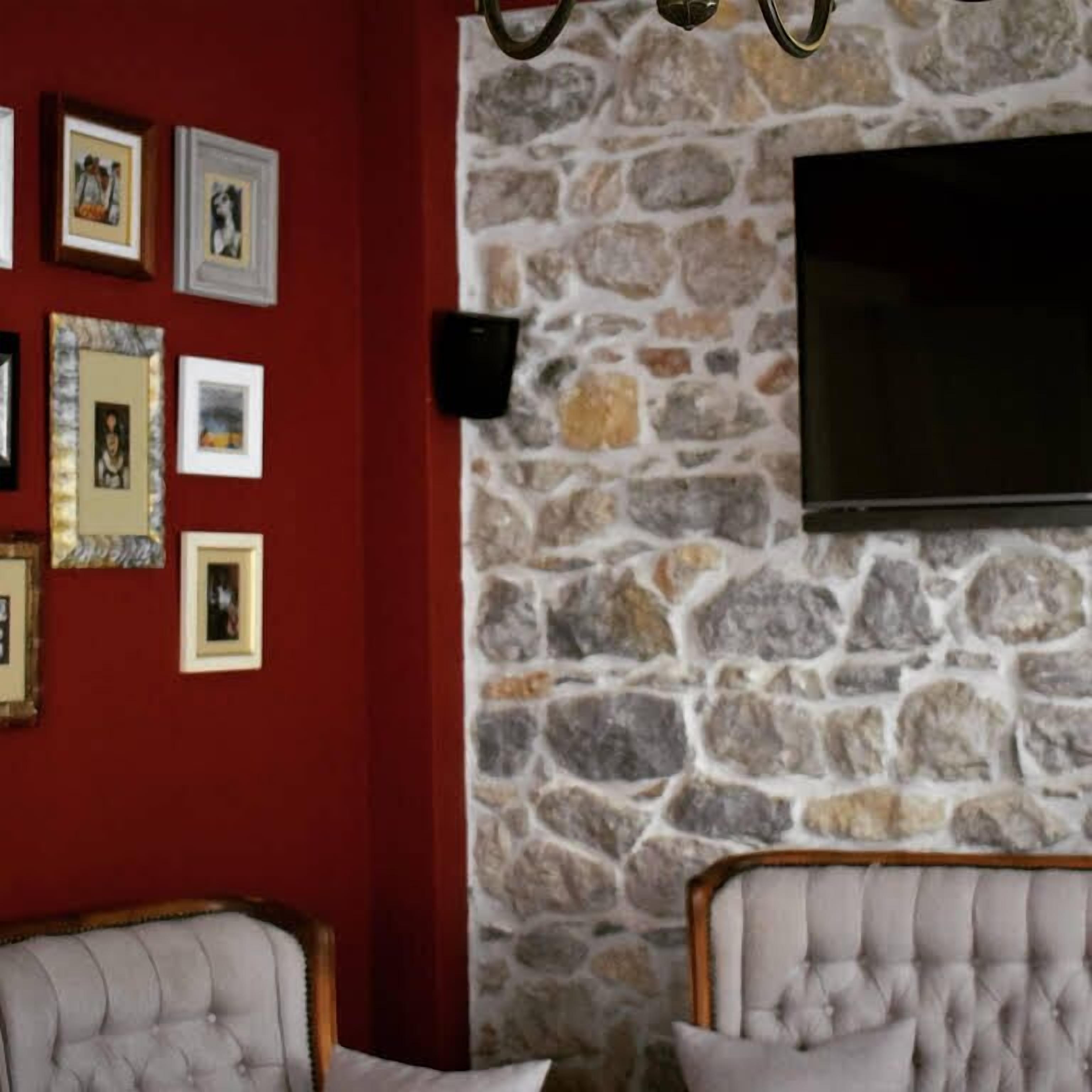 Una habitación con pared de piedra, un televisor de pantalla plana montado encima y varias fotografías enmarcadas en la pared.