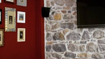 Una habitación con pared de piedra, un televisor de pantalla plana montado encima y varias fotografías enmarcadas en la pared.