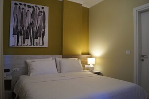 A hotel room with a bed, a nightstand with a lamp, a wall-mounted artwork, and a door.