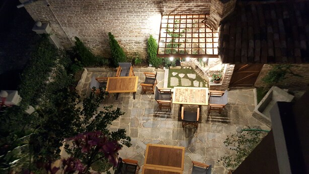 An outdoor patio with stone flooring, wooden furniture, and a brick wall. - Vila Trebicka (Korçë)
