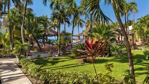 A tropical resort with palm trees, a pool area, and a thatched-roof structure. - Deluxe Beachfront Ground Floor Apartment # 6 Nautibeach (Isla Mujeres)