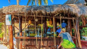 A rustic thatched-roof bar with wooden seating and a counter. - Deluxe Beachfront Ground Floor Apartment # 6 Nautibeach (Isla Mujeres)