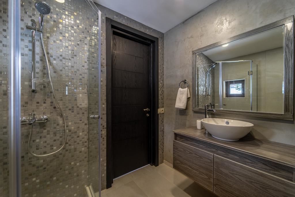 A modern bathroom with a glass-enclosed shower, a large mirror, and a wooden vanity.