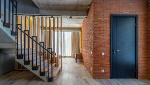 Una escalera de madera con barandillas negras que conduce a una habitación con pared de ladrillo y una puerta negra.