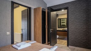 Un dormitorio moderno con cama, armario de madera y baño visible a través de una puerta abierta.