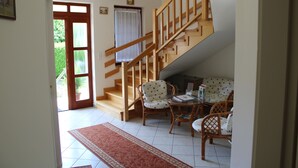 A spacious living area with a wooden staircase, a dining table with chairs, and a large window with curtains. - Erika Apartmanházak (Hévíz)