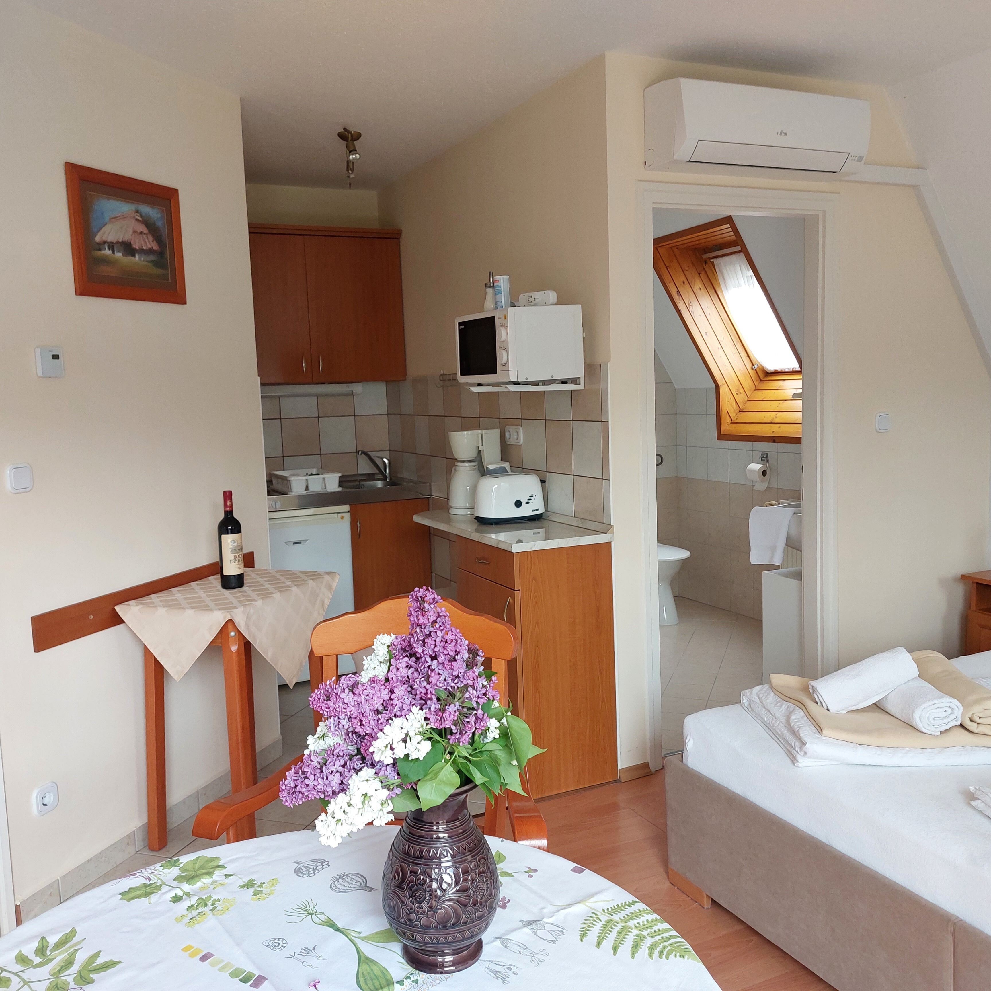 A compact kitchenette with a microwave, toaster, and sink. There's a dining area with a table and a chair, and a small bed with towels.