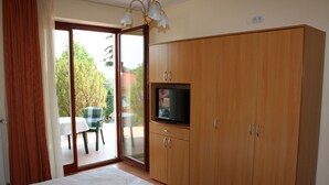 A bedroom with a bed, a television on a wooden cabinet, and a sliding glass door leading to an outdoor area with a table and chairs. - Erika Apartmanházak (Hévíz)