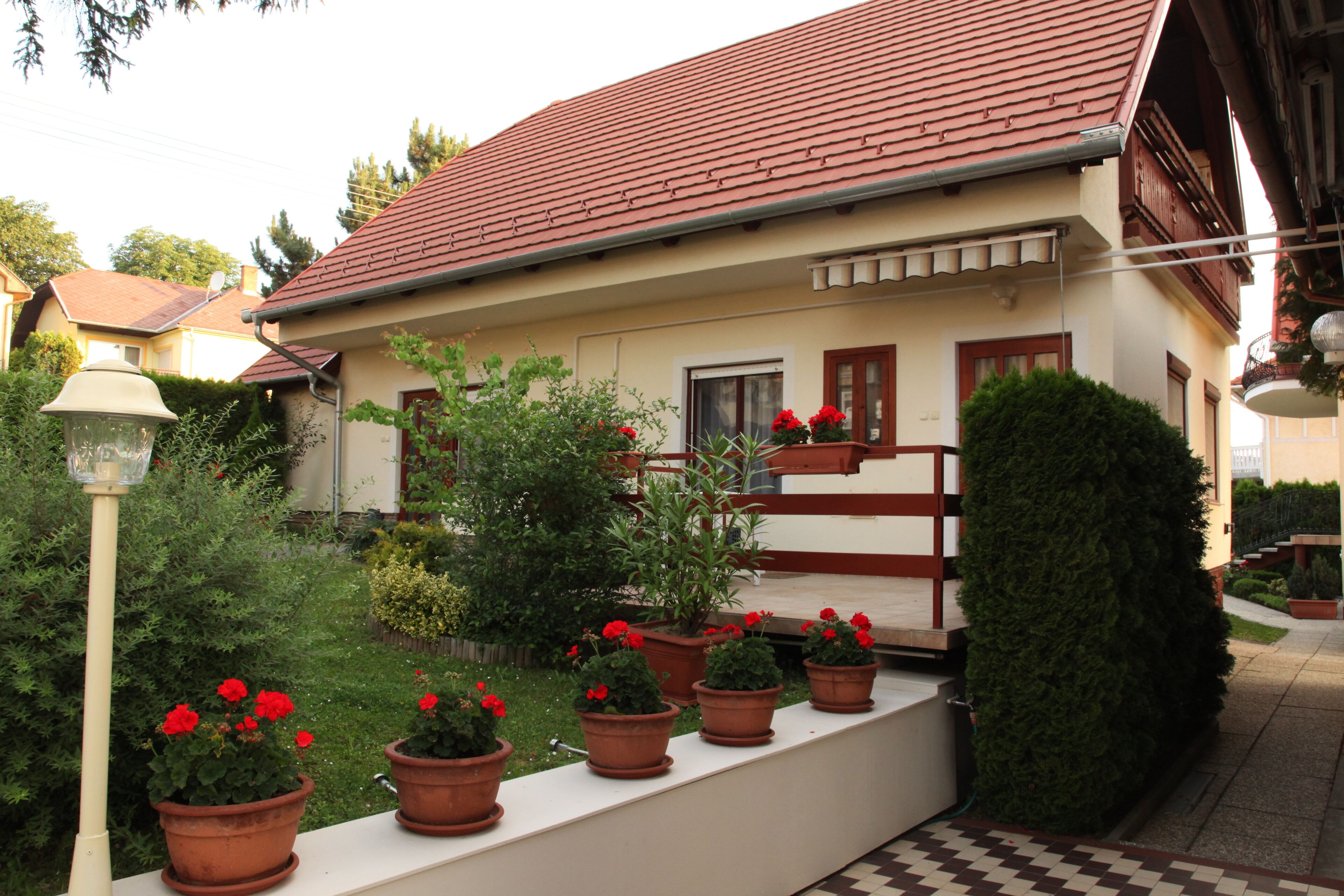 A house with a red-tiled roof, a white exterior, and a small front porch with potted red flowers.
