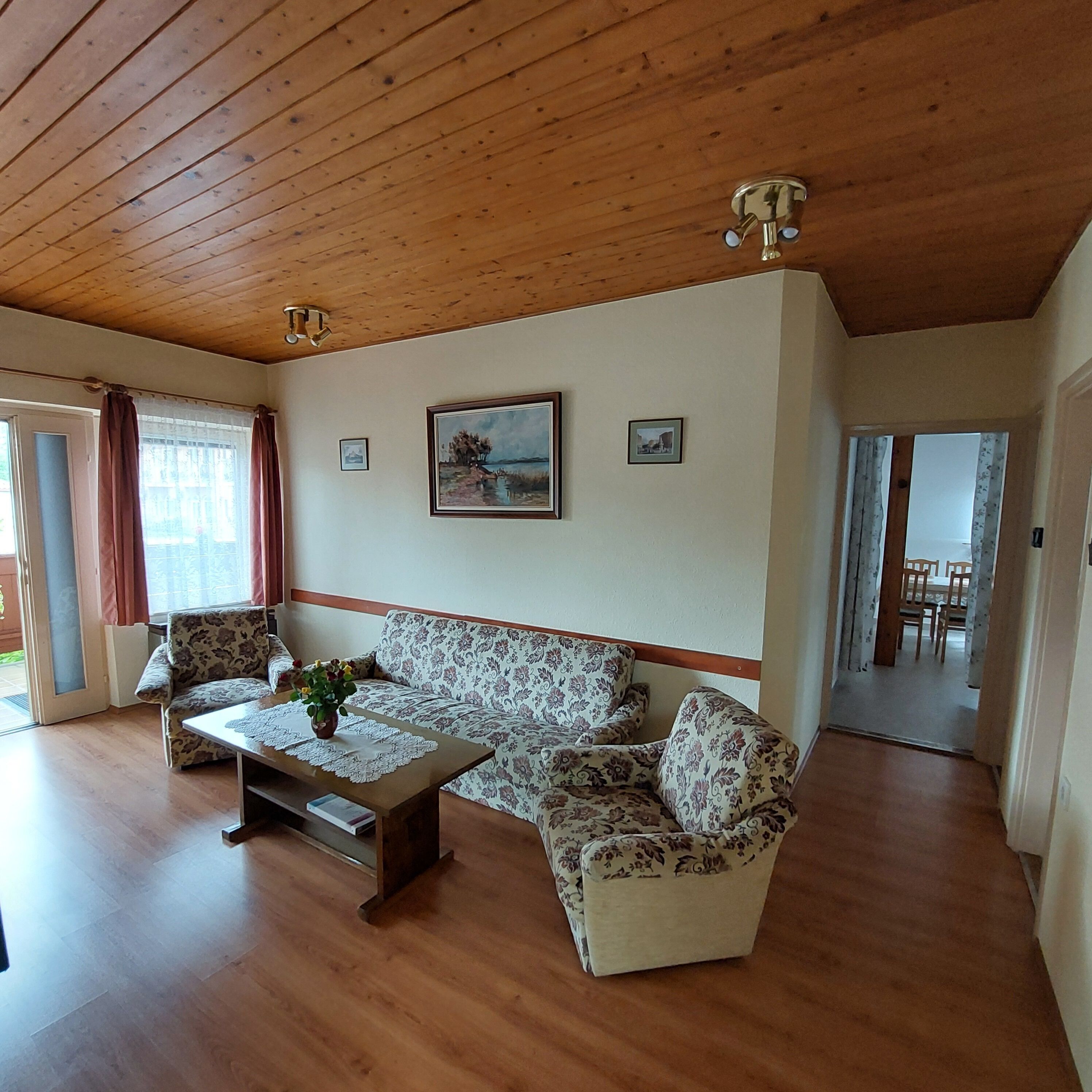A living room with a wooden ceiling, a sofa, a coffee table with a plant, and a painting on the wall.