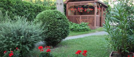 A garden with potted red flowers, a wooden gazebo, and a well-maintained lawn.