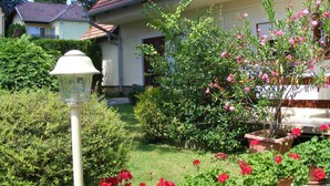A house with a red roof, surrounded by a well-maintained garden with various plants and flowers. - Erika Apartmanházak (Hévíz)