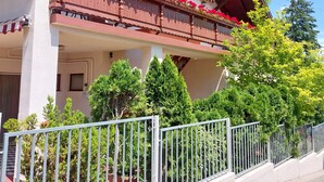 A two-story building with a balcony adorned with red flowers, a white facade, and a red roof. - Erika Apartmanházak (Hévíz)