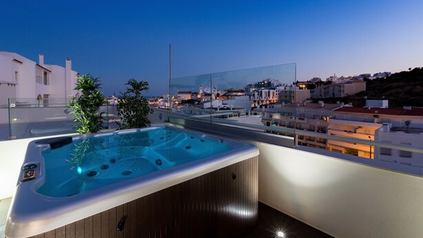A rooftop with a hot tub, glass railing, and a view of a cityscape at dusk. - D Loft Downtown (Albufeira)