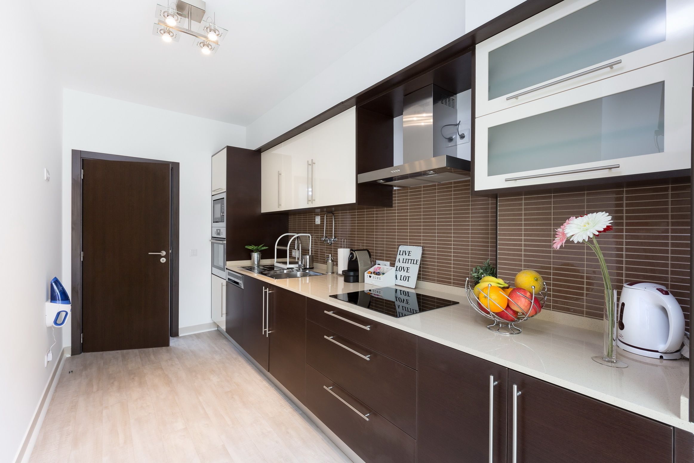 A modern kitchen with dark brown cabinets, a white countertop, and a stainless steel range hood.