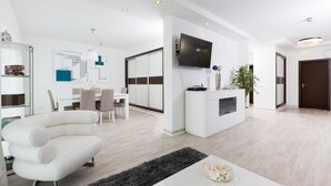 A modern living room with a white sofa, a dining area with a table and chairs, a TV mounted on the wall, and a small plant on a side table. - D Loft Downtown (Albufeira)