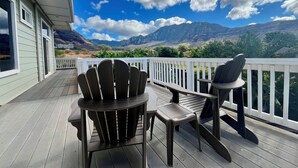 A wooden deck with Adirondack chairs and a table, overlooking a mountainous landscape. - 5 Bedroom, 6 Bath Home with Private Pool -  Ocean & Mountain Views (Waianae)