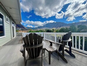 Une terrasse en bois, agrémentée de chaises Adirondack et d’une table, offrant une vue sur un paysage montagneux.