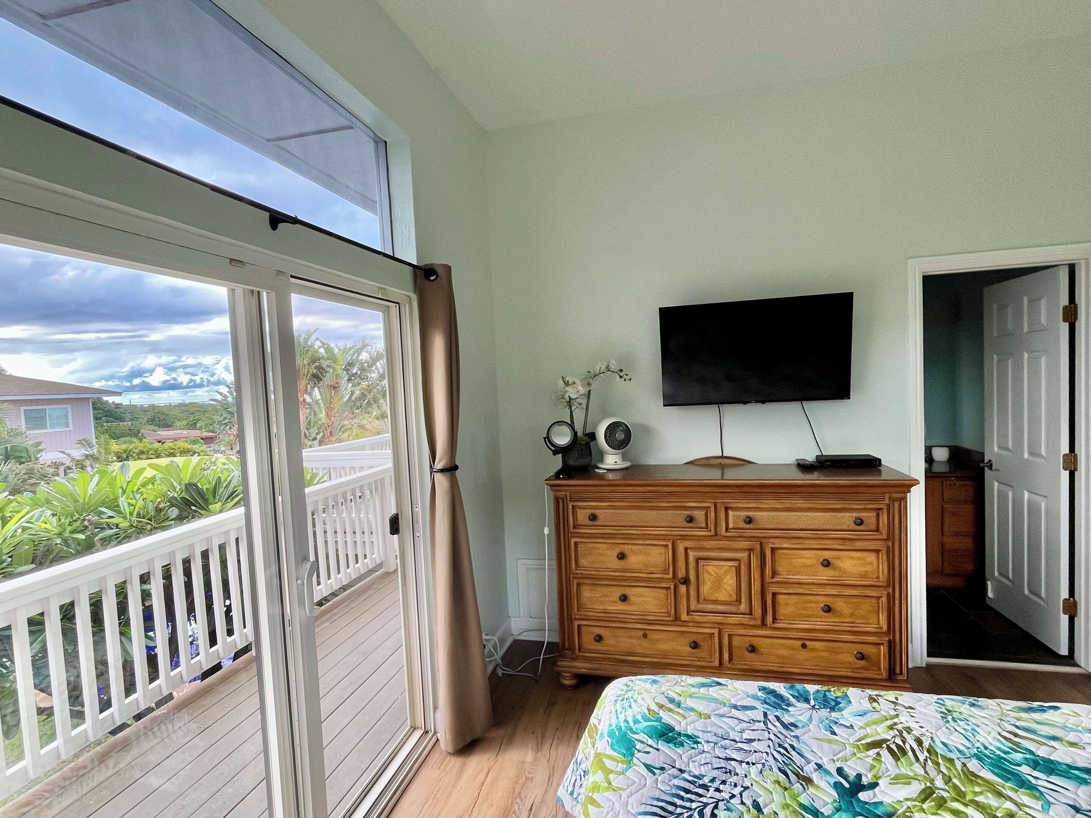 Et soveværelse med balkon, en trækommode, et fladskærms-tv og en seng med blomstret dyne.