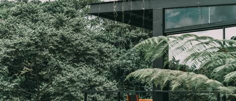 A modern outdoor seating area with a table and chairs, surrounded by dense foliage and a metal railing.