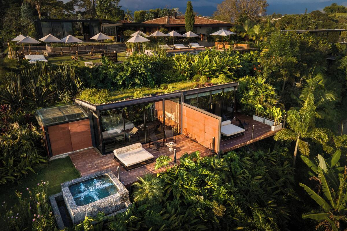 A modern outdoor living area with a glass-enclosed patio, lounge chairs, and a hot tub.