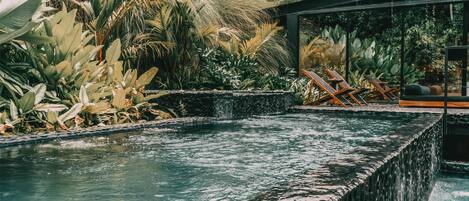 A pool with a waterfall feature, surrounded by lush tropical plants and a modern outdoor seating area.