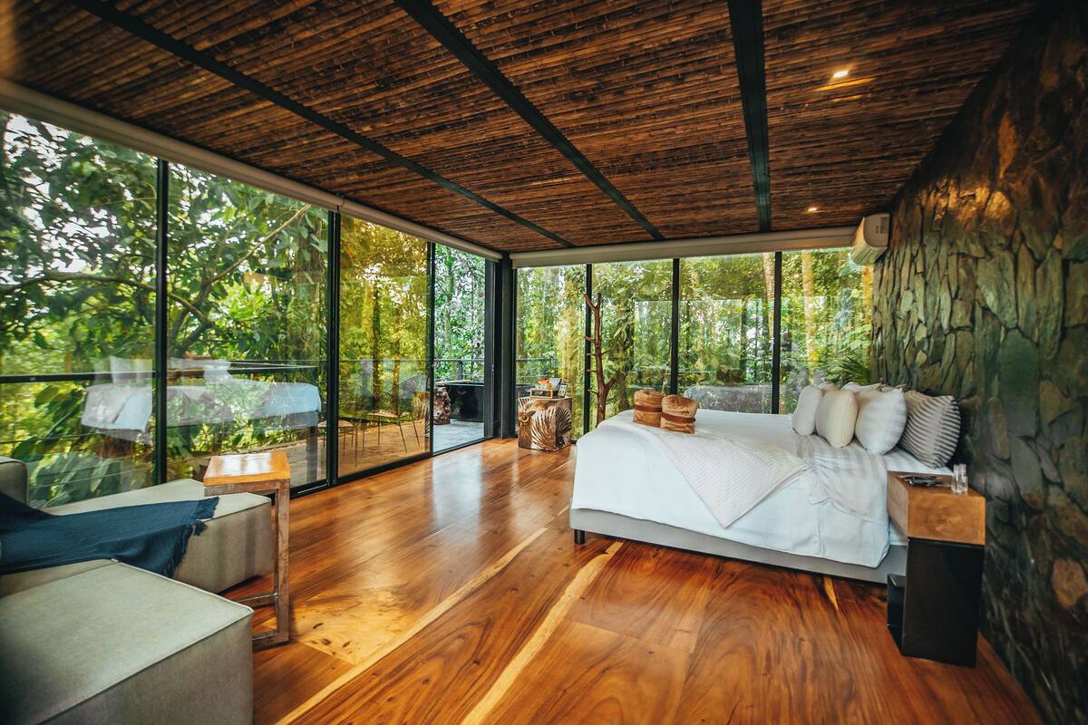 A modern bedroom with a large bed, wooden flooring, and a stone wall.