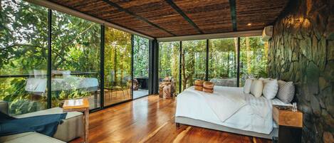 A modern bedroom with a large bed, wooden flooring, and a stone wall.