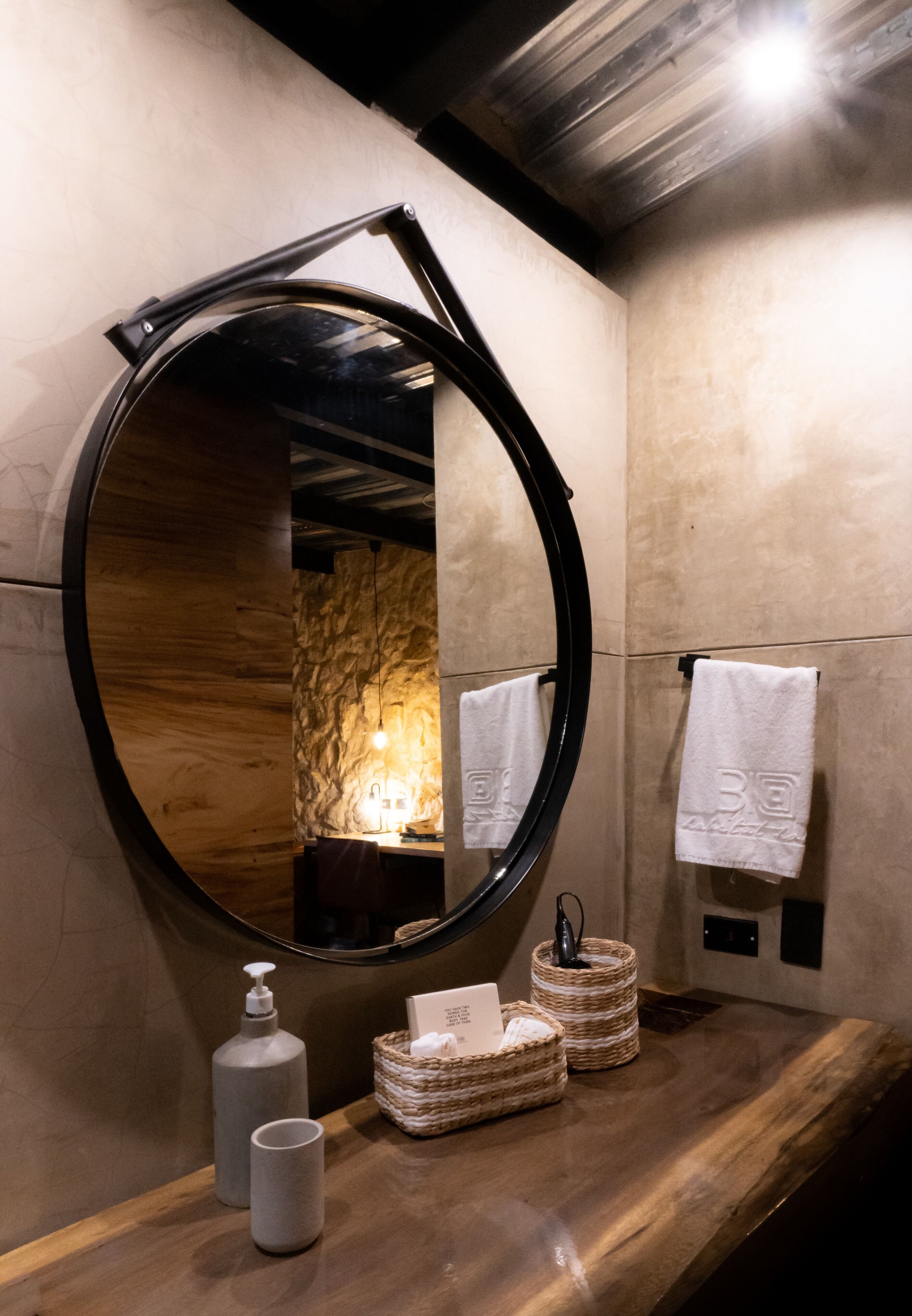 A bathroom with a wooden vanity, a round mirror, a towel rack, and a bottle of soap.